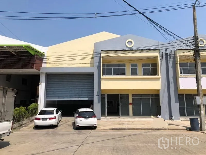 Factory for rent in Khlong Luang, Pathum Thani - Two-storey factory exterior in Khlong Luang with a large roller shutter, parking bays, and a wide driveway.