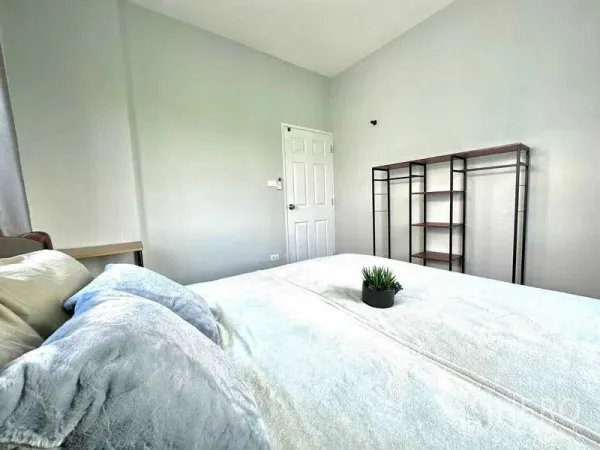 บ้าน ให้เช่าในLat Krabang, Bangkok - มุมห้องนอนเห็นเตียง ประตู และชั้นเหล็กเปิดโล่งบนผนังสีอ่อน