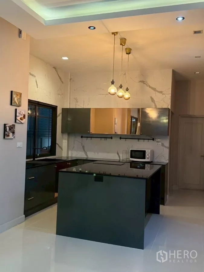 Detached House for rent or sale in Bang Phli, Samut Prakan - Modern kitchen with central island and brass pendant lights against marble walls.