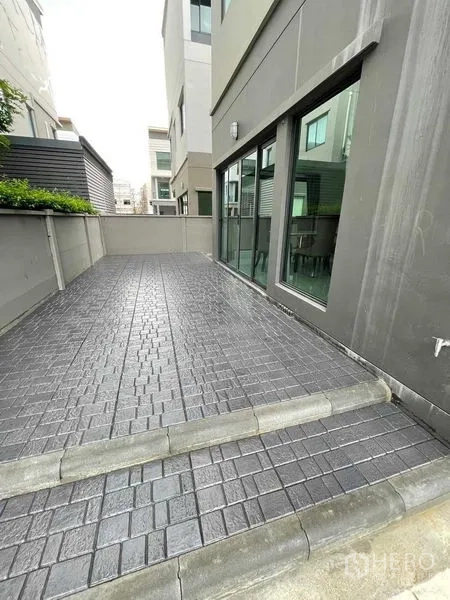 独立式住宅 出租在Khan Na Yao, Bangkok - 现代三层独栋别墅的侧面露台，铺装地面与推拉落地窗。