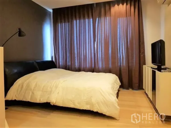 Condominium for rent in Khlong Toei, Bangkok - Cozy bedroom with large bed, blackout curtains, bedside lamp, and TV cabinet.
