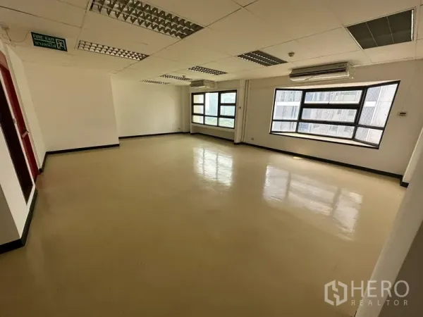 办公空间 出租在Pathum Wan, Bangkok - 转角办公区，环绕窗户、紧急出口标识与壁挂空调。