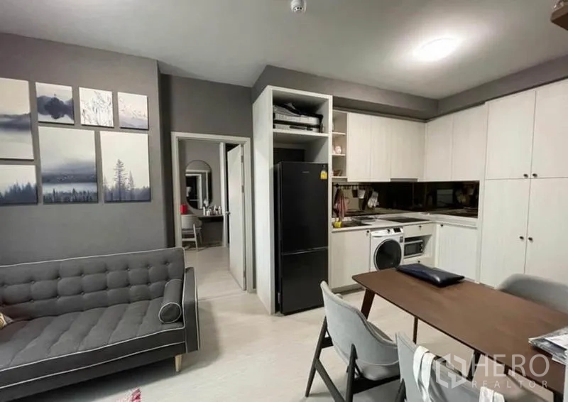 Condominium for sale in Bang Sue, Bangkok - Open-plan living area with dining table and white fitted kitchen with black fridge.