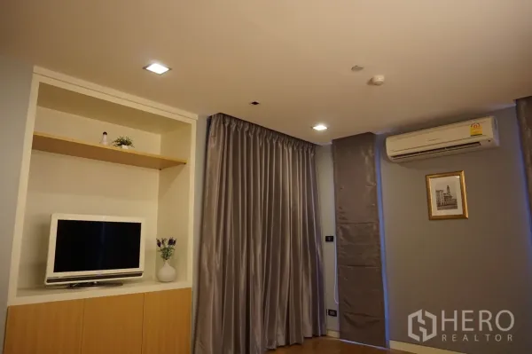 Condominium for rent or sale in Bang Rak, Bangkok - Bedroom corner with built-in TV cabinet, floor-to-ceiling curtains and an AC unit for a cozy retreat.