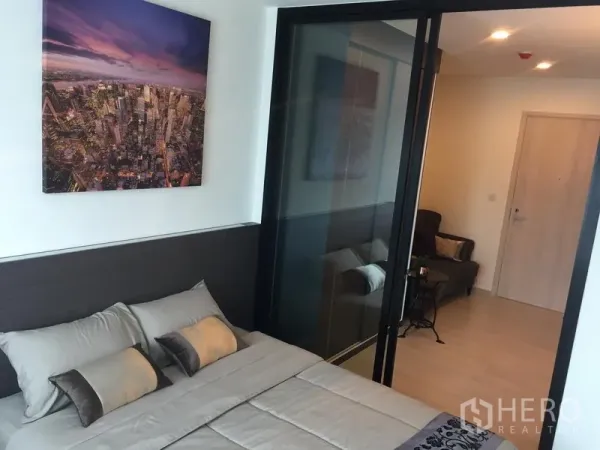 Condominium for rent in Huai Khwang, Bangkok - Bedroom with double bed, cityscape artwork and glass sliding partition opening to the living room.