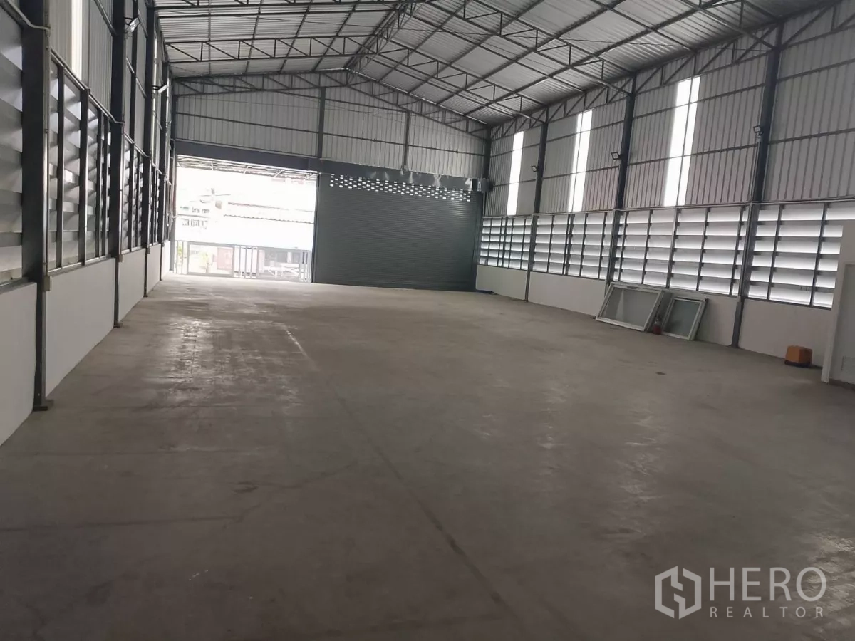 Warehouse for rent in Huai Khwang, Bangkok - Spacious warehouse interior with high gable roof and louvered windows, view to front door.