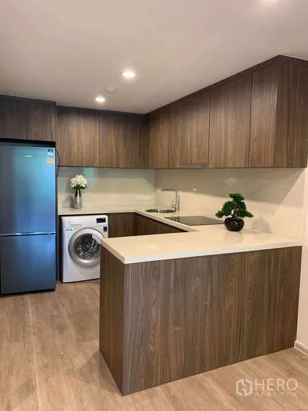 Condominium for rent - Modern L-shaped kitchen with wood cabinetry, quartz counters, stainless refrigerator and in-unit washer at Noble Above Wireless.