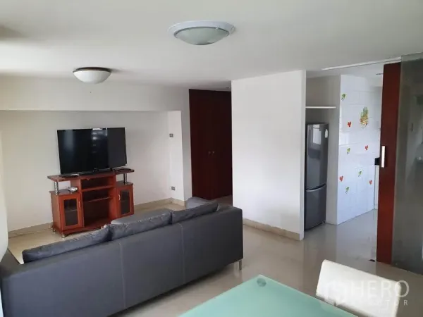 公寓 出售在Watthana, Bangkok - 开放式客厅视角，灰色沙发与电视，通向独立厨房。