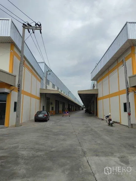 Warehouse for rent in Krathum Baen, Samut Sakhon - Wide truck-friendly lane between two warehouse buildings with long canopies.