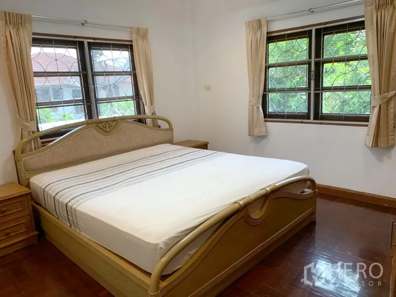 Detached House for rent in Khlong Toei, Bangkok - Spacious bedroom with large bed, twin windows, curtains and wooden flooring.