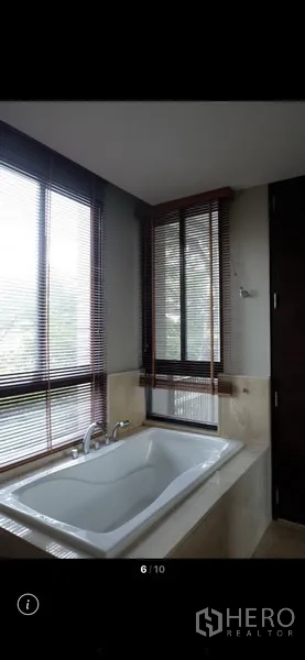 Condominium for rent in Watthana, Bangkok - Bathroom with a soaking bathtub set by corner windows with blinds and views of surrounding trees.
