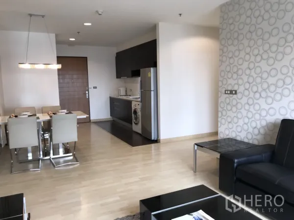 Condominium for rent in Watthana, Bangkok - Dining area beside a compact kitchenette with fridge and washing machine, set against patterned feature walls.