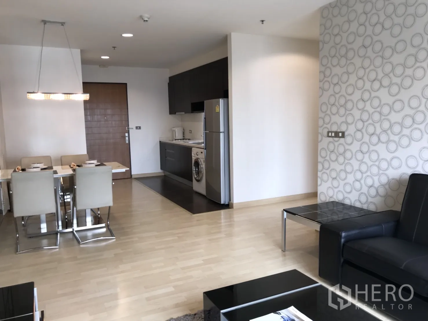 Condominium for rent in Watthana, Bangkok - Dining area beside a compact kitchenette with fridge and washing machine, set against patterned feature walls.