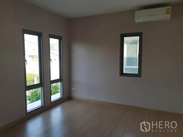 Detached House for sale in Nonthaburi - Empty bedroom with slim vertical windows, air conditioner and wood floors.