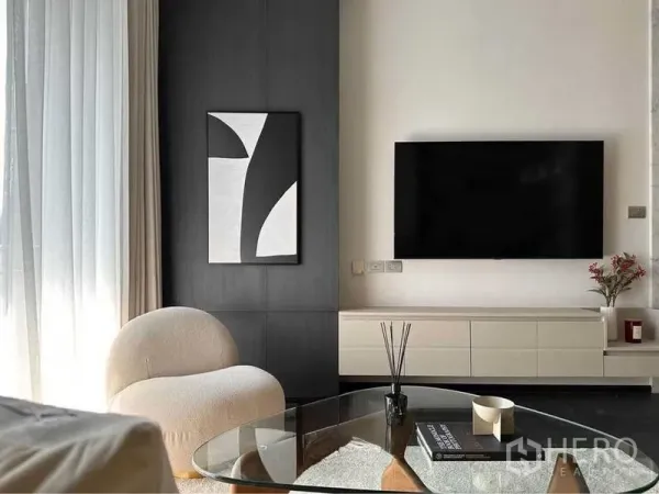 Condominium for rent or sale in Watthana, Bangkok - Bright living room with abstract art, wall-mounted TV, glass coffee table and lounge chair.