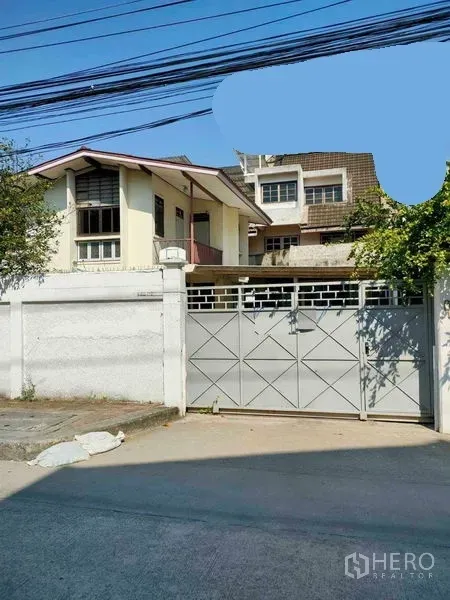 零售空间 出租在Yan Nawa, Bangkok - 街边高墙与金属推拉门，院内可见双层斜屋顶建筑与绿植，临混凝土道路。