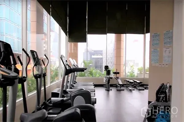 Condominium for rent in Bang Rak, Bangkok - Fitness center with cardio machines beside floor-to-ceiling windows overlooking the city.