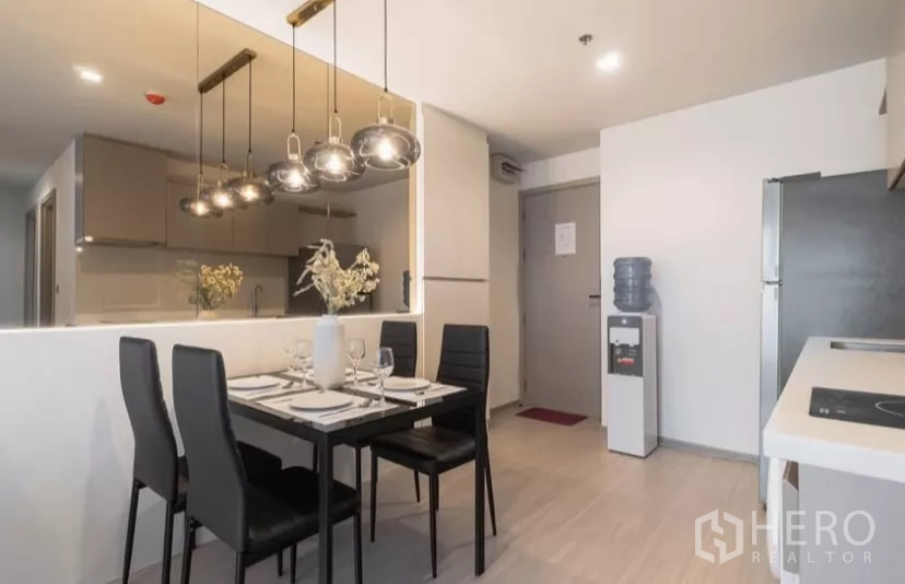Condominium for rent in Chatuchak, Bangkok - Dining table for four beside the open kitchen with pendant lamps, refrigerator and entry door.