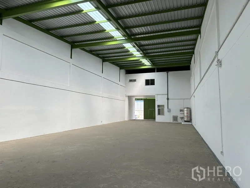 Warehouse for rent in Pathum Thani - Open warehouse floor facing main entrance, high ceiling and translucent roof panels for daylight.
