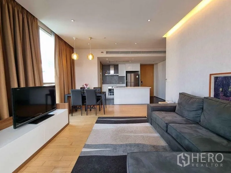 Condominium for rent in Watthana, Bangkok - Open-plan living and dining area with sofa, TV and kitchen island by large windows.