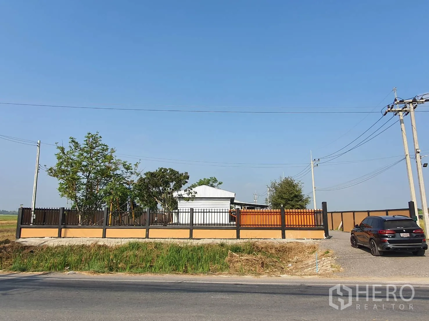 Warehouse for sale in Lam Luk Ka, Pathum Thani - Front boundary wall and entrance gate facing a paved public road.