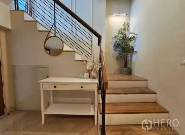 Townhouse for rent - Entry landing featuring wooden stairs, black railings, a console table, and a round mirror.