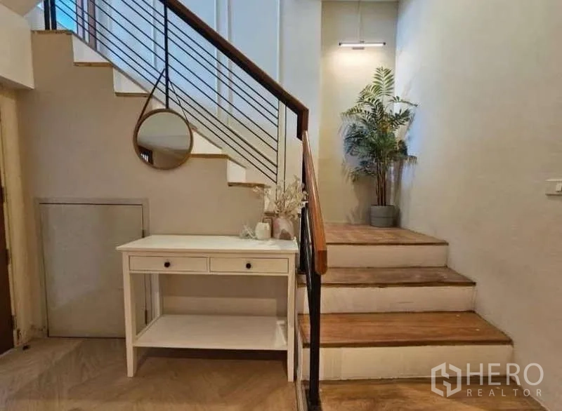 Townhouse for rent - Entry landing featuring wooden stairs, black railings, a console table, and a round mirror.