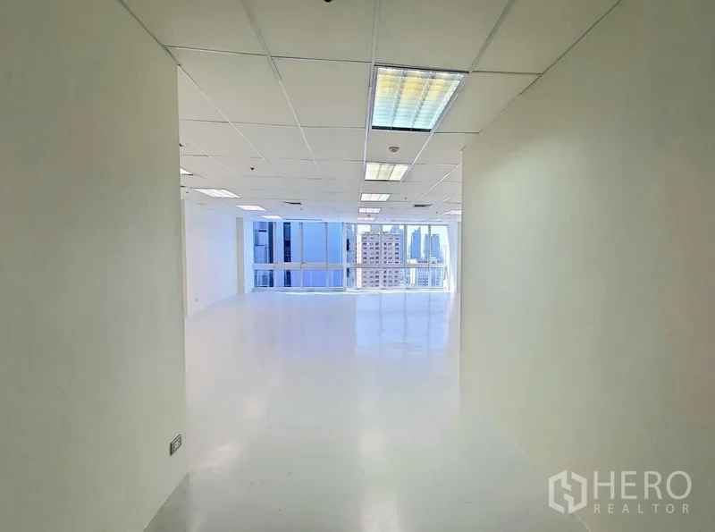 Office Space for rent in Khlong Toei, Bangkok - Bright entry corridor opening to an open‑plan office with white floors, drop‑ceiling lights, and large windows showing Bangkok skyline views.