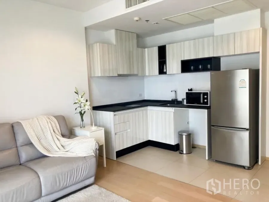 Condominium for rent in Watthana, Bangkok - Bright open-plan living room with L-shaped kitchen, stainless refrigerator and sofa in a Bangkok condo.