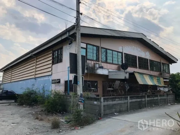货栈 出租在Nonthaburi - 建筑侧后方，二层长窗与小阳台，周边围墙与巷道。