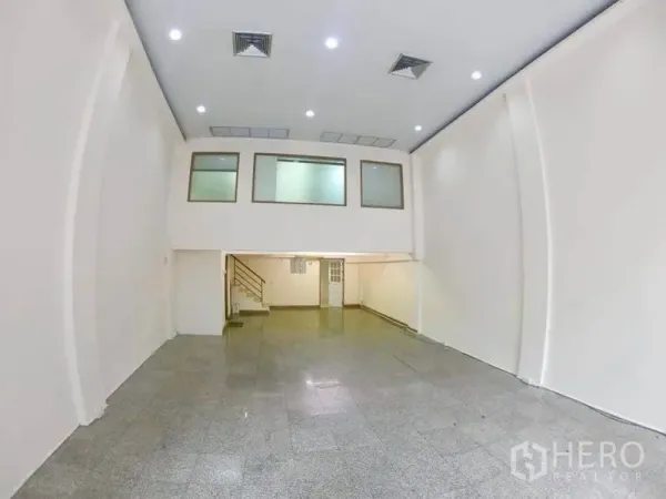 Office Space for rent in Khlong Toei, Bangkok - Double-height showroom-style office with mezzanine, recessed lights and a staircase.