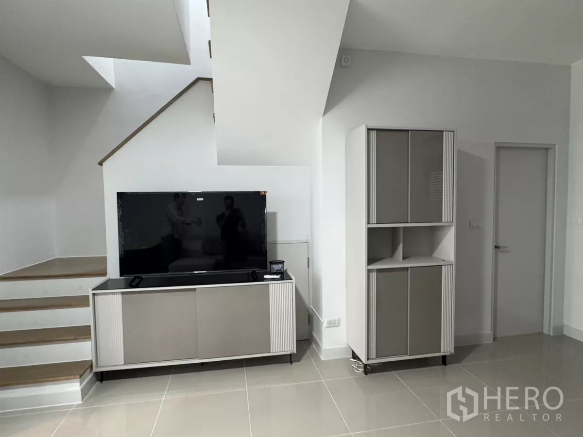Townhouse for rent in Bang Phli, Samut Prakan - TV console beside the staircase in a minimalist white interior.