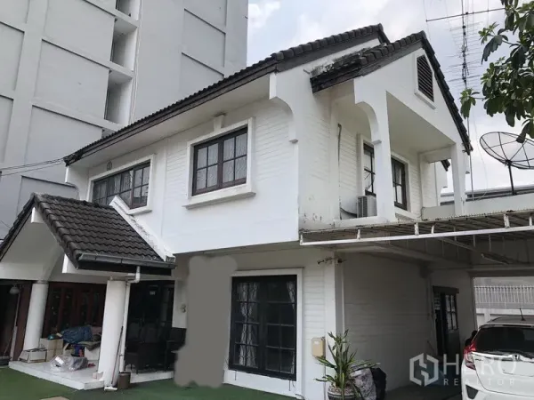 独立式住宅 出售在Pak Kret, Nonthaburi - 靠近立面的两层房屋，斜瓦屋顶，阳台与有顶车棚。