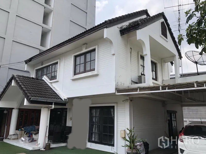 独立式住宅 出售在Pak Kret, Nonthaburi - 靠近立面的两层房屋，斜瓦屋顶，阳台与有顶车棚。