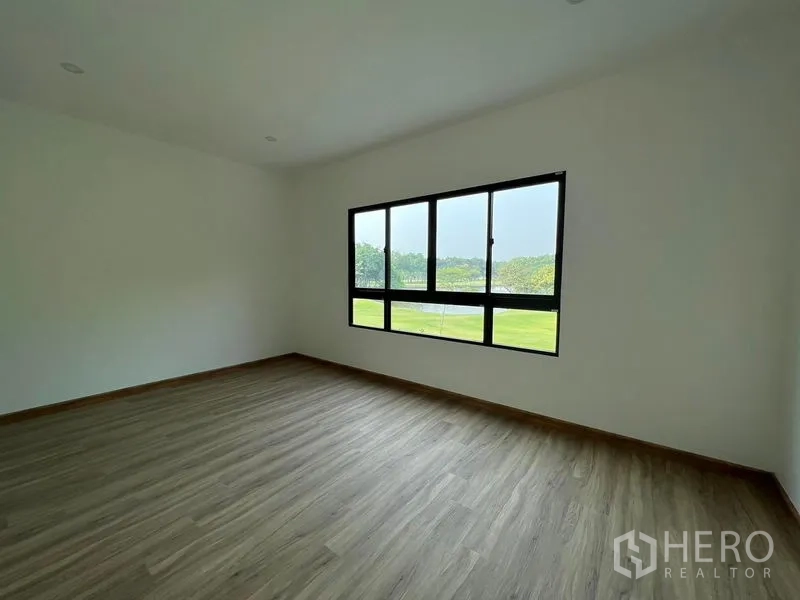 Townhouse for rent in Bang Kapi, Bangkok - Expansive bedroom with laminate floor and long horizontal window facing a green field.