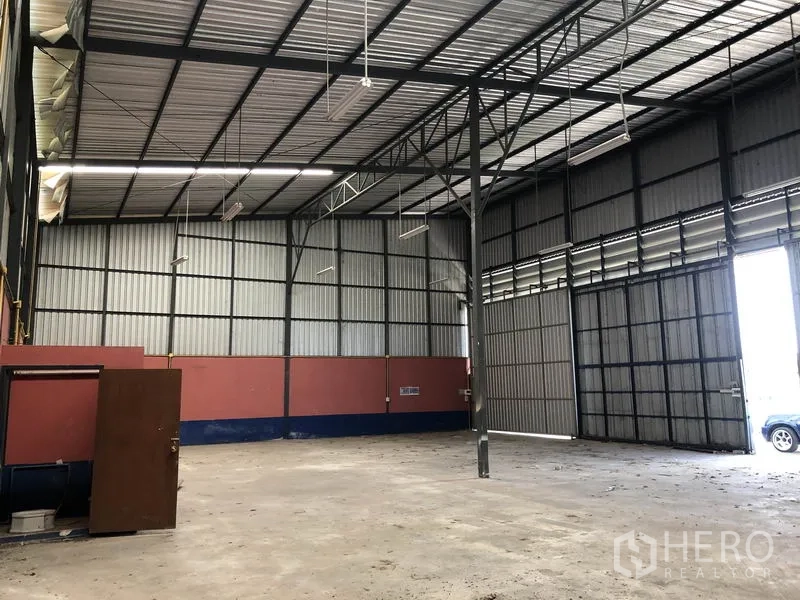 Warehouse for rent in Lam Luk Ka, Pathum Thani - Warehouse interior showing large sliding entrance, steel columns, corrugated walls and open storage floor.