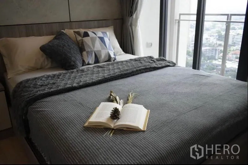 公寓 出租或出售在Phaya Thai, Bangkok - 卧室铺灰色床品，阳台门外可见城市天际线。