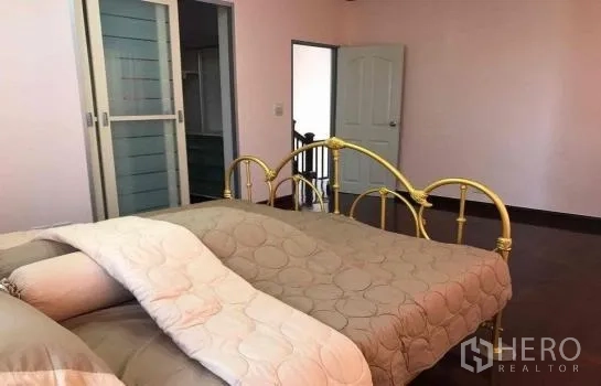 Detached House for rent in Khlong Sam Wa, Bangkok - Spacious master bedroom with a brass bedframe, pastel walls and sliding closet doors.
