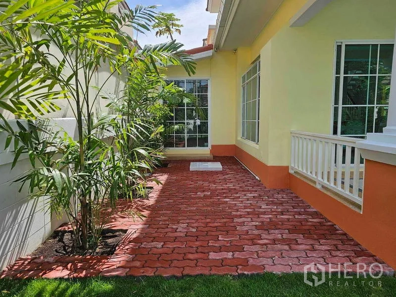 Detached House for rent in Thanyaburi, Pathum Thani - Brick-paved side patio with tropical plants and floor-to-ceiling sliding windows.