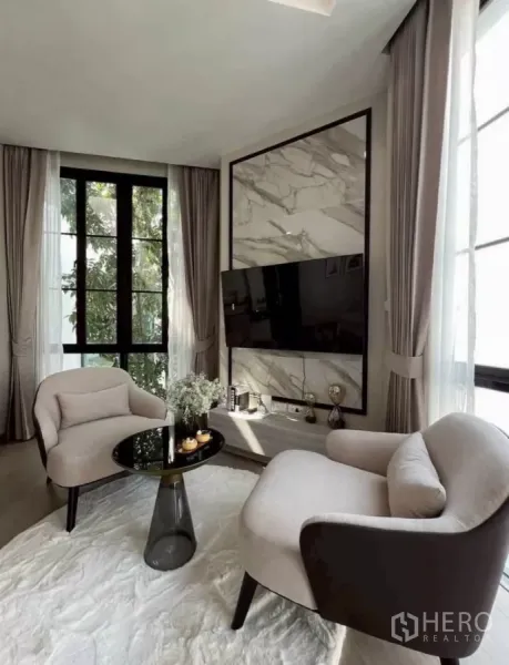 独立式住宅 出租在Lat Phrao, Bangkok - 舒适休闲角，两把扶手椅、岩板电视背景墙与落地窗。