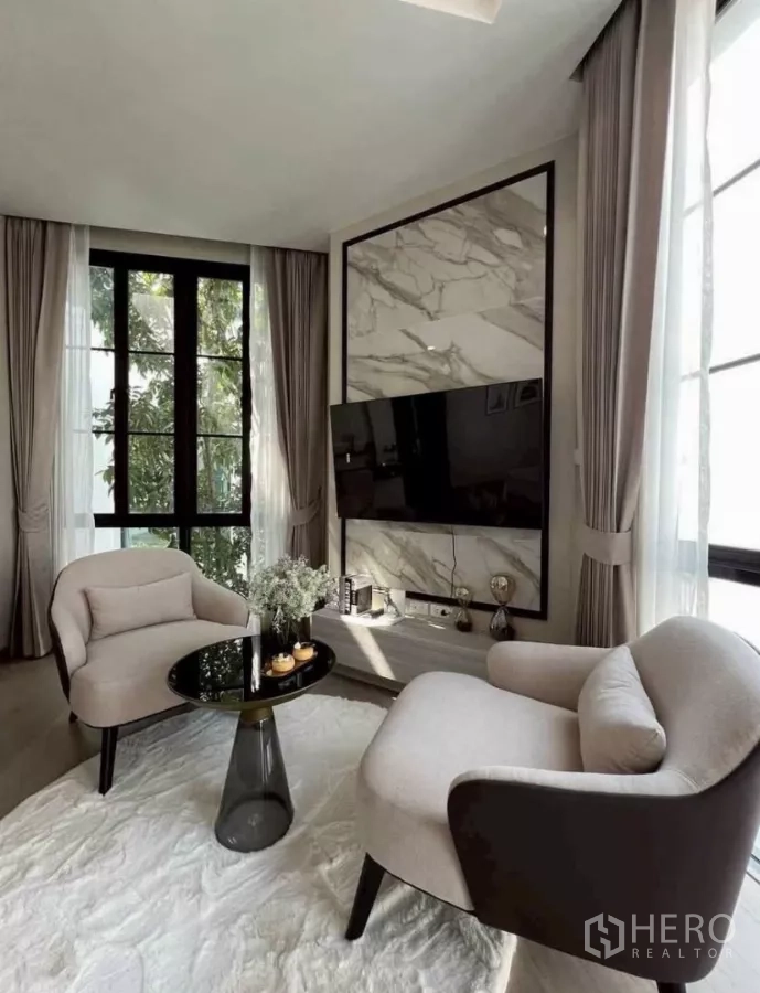 独立式住宅 出租在Lat Phrao, Bangkok - 舒适休闲角，两把扶手椅、岩板电视背景墙与落地窗。