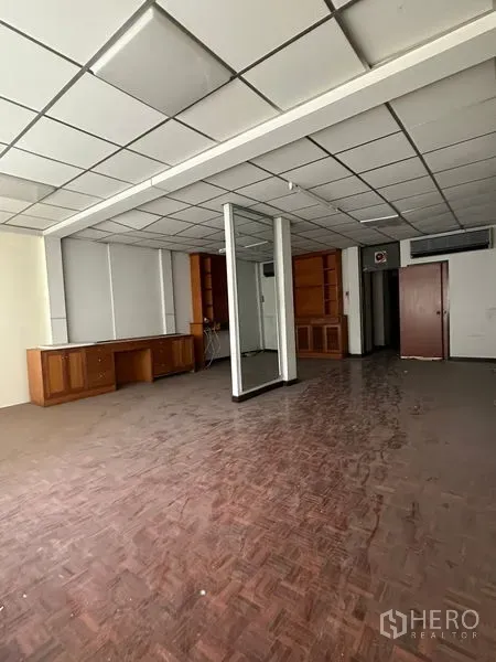 Shophouse for rent in Sathon, Bangkok - Large open-plan office floor with mirrored column, parquet floors, and built-in storage units.