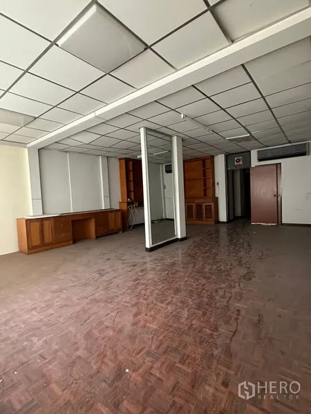 Shophouse for rent in Sathon, Bangkok - Large open-plan office floor with mirrored column, parquet floors, and built-in storage units.