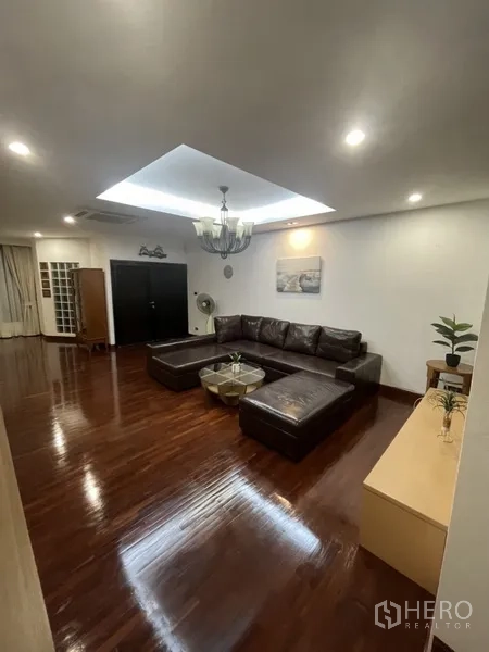 Home Office for rent or sale in Phra Khanong, Bangkok - Spacious living room with leather sectional, wooden floors and recessed ceiling lighting.