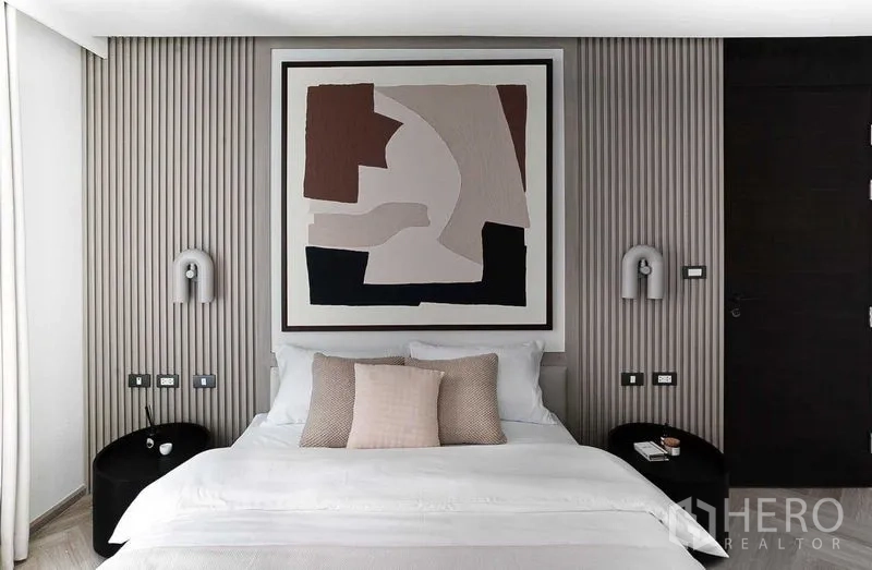 คอนโด ขายในRatchathewi, Bangkok - ภาพใกล้เตียงนอนใหญ่ มีโคมไฟข้างเตียง ผนังลอนและงานศิลป์นามธรรม