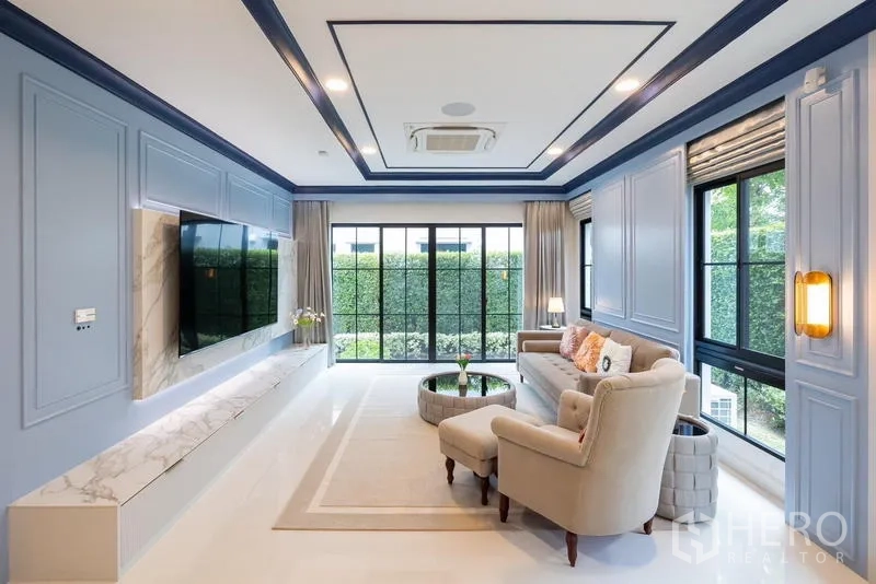 Detached House for sale in Saphan Sung, Bangkok - Spacious living room with blue panelled walls, marble TV wall and garden view.