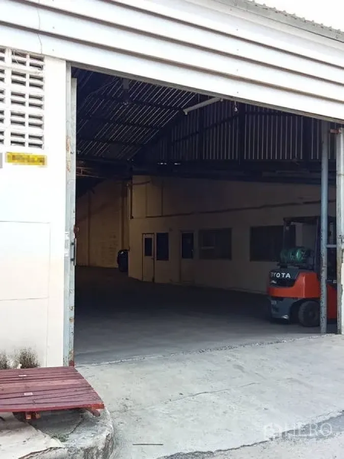 คลังสินค้า ให้เช่าในMueang Samut Prakan, Samut Prakan - ทางเข้าโกดังแบบประตูม้วน เปิดสู่ภายใน เห็นรถโฟล์คลิฟท์และโครงหลังคาเหล็ก