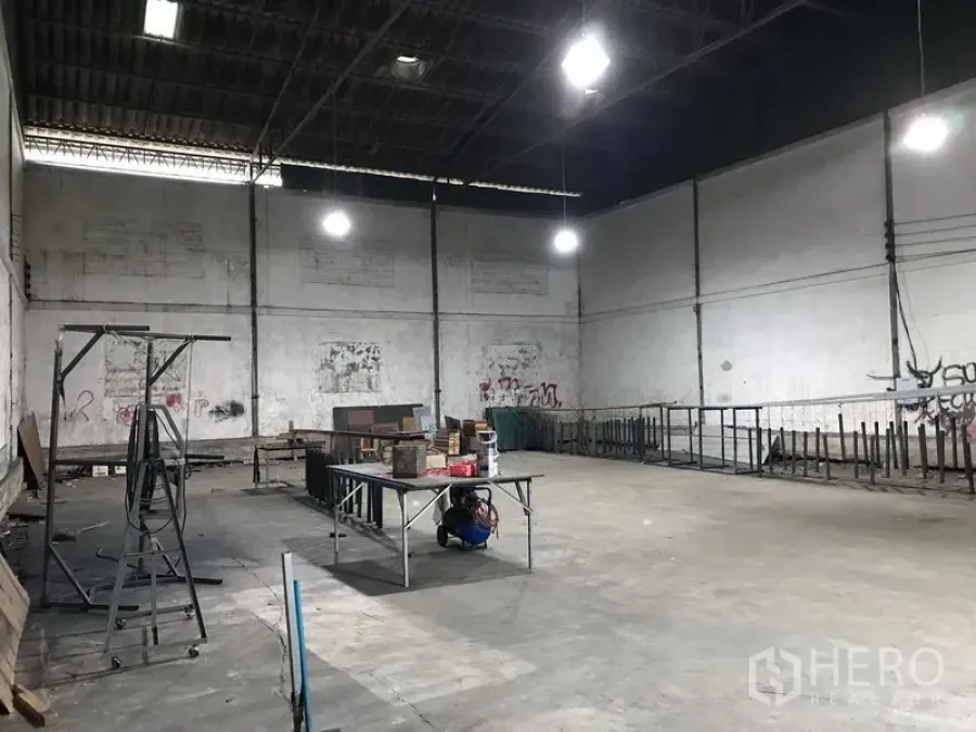 Warehouse for rent in Bang Phli, Samut Prakan - Spacious warehouse interior in Bang Phli with high steel roof, bright hanging lights, concrete floor and open storage area.