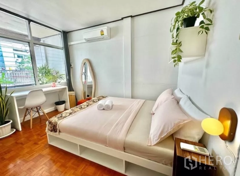 Townhouse for rent in Watthana, Bangkok - Sunlit bedroom with desk by a big window, air conditioner and indoor plants.