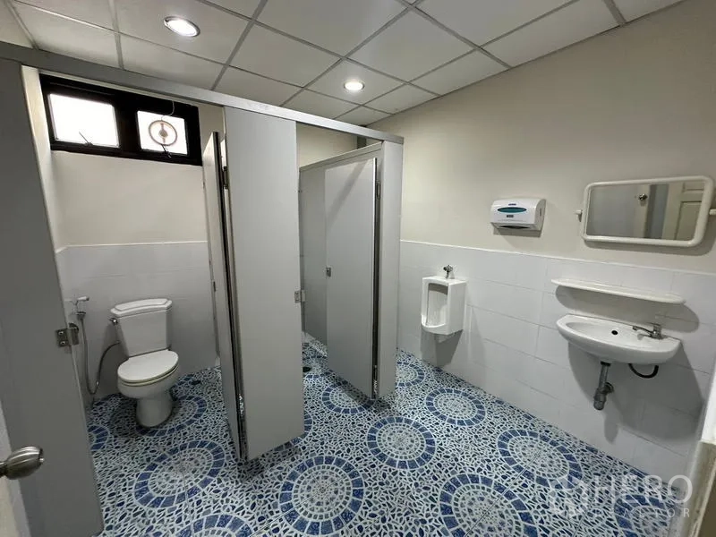Office Space for rent - Clean shared restroom with stalls, urinal, and wall-mounted sink.